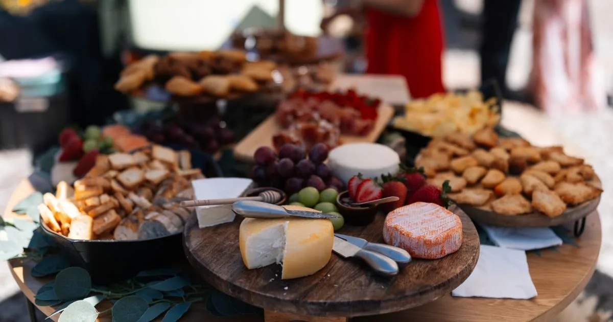 Mesa de catering Aperidrinks em Felgueiras, com tábuas de queijos, frutas frescas, pão artesanal e aperitivos servidos em ambiente de evento.