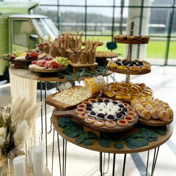 Mesa de finger food premium com doces e salgados para catering de casamentos, com a Piaggio Maria Amélia da Aperidrinks ao fundo.